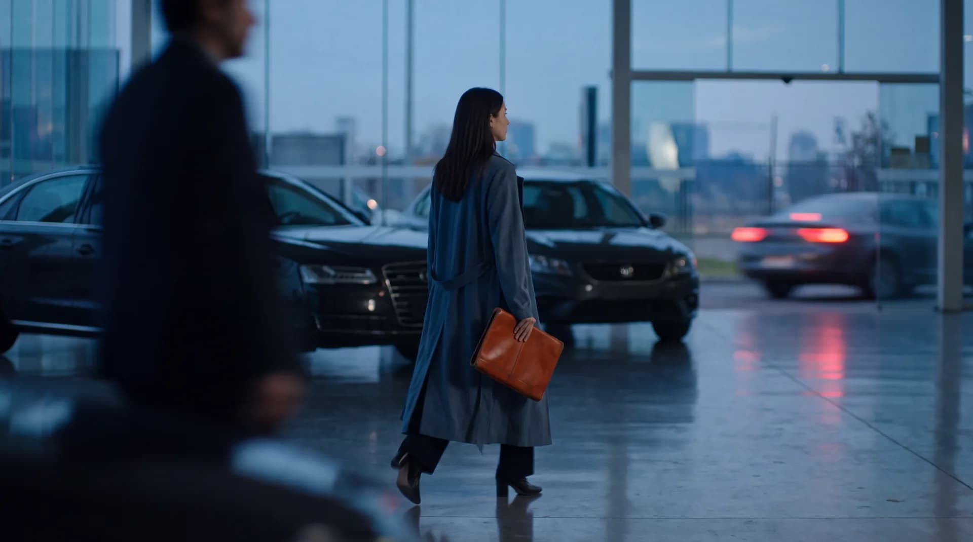 An executive walks the floor of a car dealership between two cars.